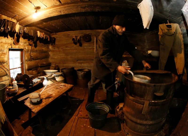 Baburin fills bucket with hot water from barrel at bath room of his house in remote Siberian village of Mikhailovka